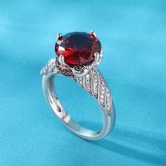 a ring with a large red stone surrounded by white diamonds on a blue cloth background