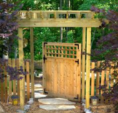 a wooden gate in the middle of a garden with purple flowers and trees around it