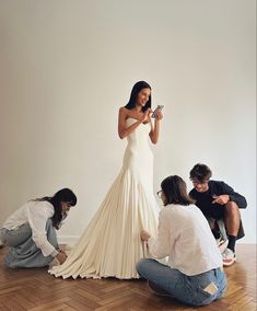 a woman in a white dress is taking pictures with her camera while three other people sit on the floor