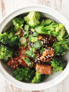 a white bowl filled with broccoli and meat covered in sesame seed flakes