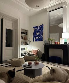 two cats laying on top of pillows in a living room next to a coffee table