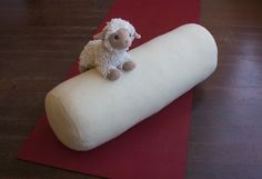 a stuffed sheep sitting on top of a rolled up roll of fabric in a room