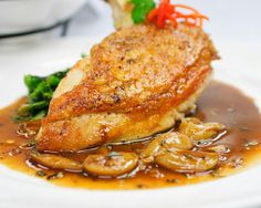 a piece of chicken with mushrooms and broccoli in gravy on a white plate