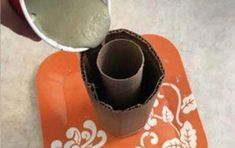 a person pouring cement into a cup on top of an orange coaster with white designs