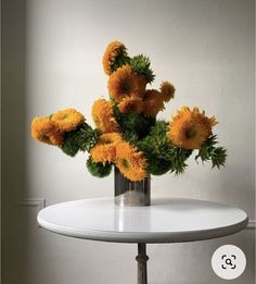 a white table topped with a metal vase filled with yellow and green flowers on top of it