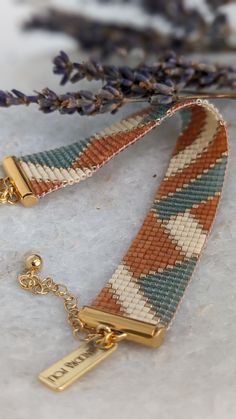 a close up of a bracelet on a table with flowers in the background and a gold plated charm attached to it