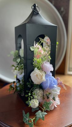 a black lantern with flowers and greenery sitting on a table next to a plate