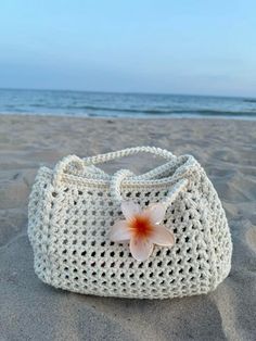 a crocheted bag with a flower on it sitting in the sand at the beach