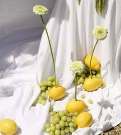 there are grapes and lemons on the table with flowers in front of white cloth