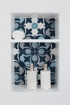 two white toiletries sitting on top of a bathroom shelf next to a blue and white tiled wall