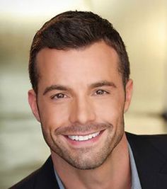 a smiling man in a black suit and blue shirt is looking at the camera with a smile on his face