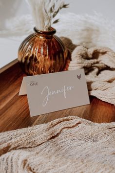 a table topped with a vase filled with flowers next to a white and brown card