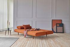 an orange couch sitting on top of a hard wood floor next to a white wall