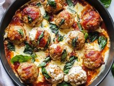 a pan filled with meatballs covered in cheese and spinach on top of a table