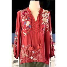 New With Tags Size Small This Deep Red Blouse By Johnny Was Is 100% Silk With A Whimsical Floral Pattern. The Longsleeve Top Has Double Tassel Ties At Its Flattering V-Neck. The Embroidery At The Bottom Features A Large White Crane. On The Front Side Is A Darting Dragonfly & The Back Shoulder Detailing Is A White Embroidered Desert Landscape. The Blouse Also Has Convenient Side Slits. In The Pictures The Top Is Paired With Anthropologie Alec Les Filles Faux Leather Green Pants Available For Sale Red Long Sleeve Top With Intricate Embroidery, Red Long Sleeve Blouse With Floral Embroidery, Red Tops With Embroidered Sleeves For Spring, Red Blouse With Embroidered Sleeves, Bohemian Red Blouse With Intricate Embroidery, Red Embroidered Blouse For Fall, Fall Embroidered Red Blouse, Black Velvet Blouse, White Embroidered Blouse