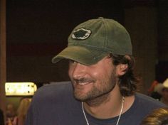 a man with a beard wearing a green hat and smiling at the camera while standing next to other people