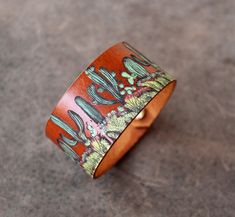 a wooden bracelet with cactus designs on the outside and inside, sitting on a concrete surface