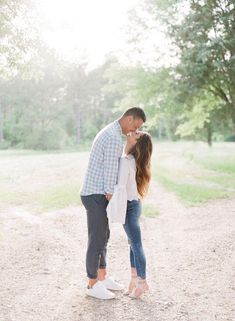 a man and woman kissing in the middle of a dirt road with trees behind them