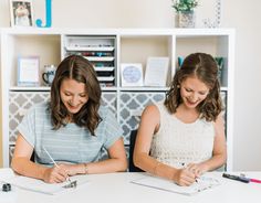 two young women sitting at a table writing on notebooks and taking notes in front of them