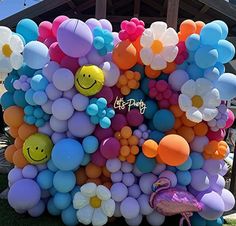 a bunch of balloons that are in the grass with a smiley face on one side and flowers on the other