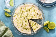 a pie with limes around it on a blue table cloth next to plates and utensils