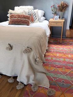 a bedroom with a bed, nightstand and colorful rugs on the floor in front of it