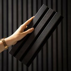 a woman's hand is holding a piece of black wood that has vertical strips on it