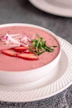 a white plate topped with a bowl of soup and garnished with sliced strawberries