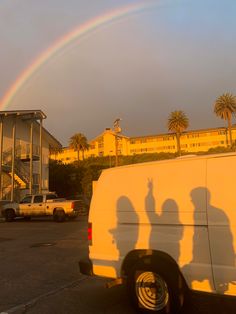 two people standing in front of a white van with a rainbow behind them and palm trees