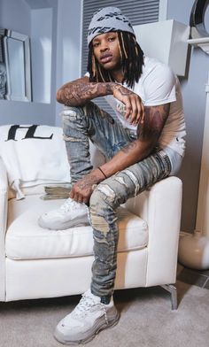 a man with dreadlocks sitting on a couch in a living room next to a white chair