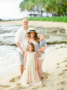 a family standing on the beach in front of water and palm trees with their baby girl