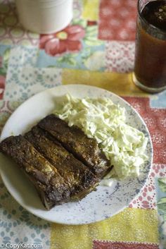 a white plate topped with meat and cole slaw next to a glass of soda