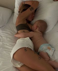 a woman laying on top of a bed next to a baby in a diaper