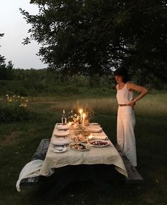 a woman standing next to a table with food on it in the middle of a field