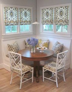 a dinning room table with four chairs around it and two windows in the background