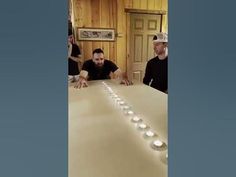 three men are sitting at a table with candles on it and one man is standing in front of the table