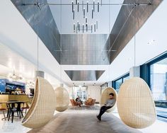 a person is walking through an office lobby with hanging chairs and lamps on the ceiling