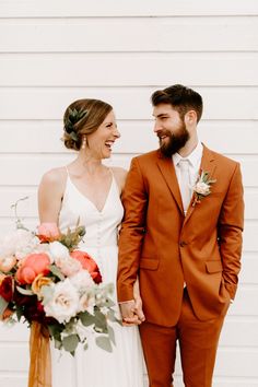 a bride and groom smile at each other as they stand in front of a white wall