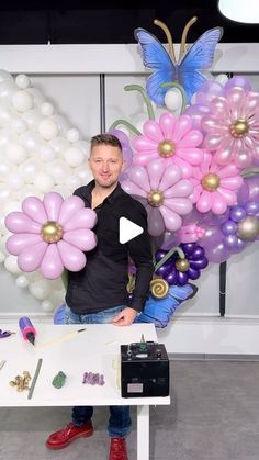 a man standing in front of a table with balloons and flowers on it while holding a camera