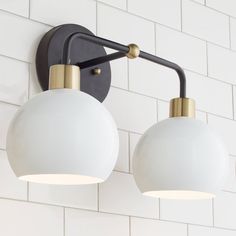 two light fixtures mounted on the wall in a white tiled room with black and gold accents