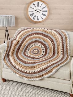 a crocheted blanket on a couch with a clock in the corner behind it