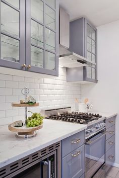 a kitchen with gray cabinets and marble counter tops, stainless steel appliances and white subway backsplash