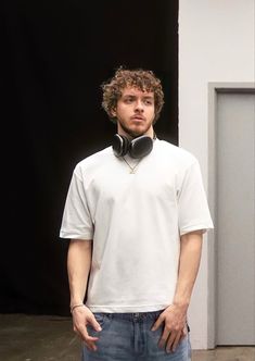 a man standing in front of a black door wearing headphones with his hands on his hips