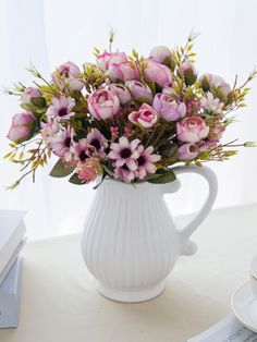 a white vase filled with pink flowers on top of a table next to a cup and saucer