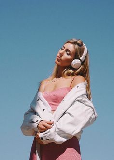 a woman in a pink dress with headphones on her ears looking off into the distance