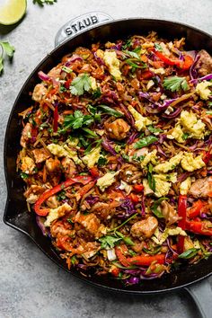 a skillet filled with meat and vegetables on top of a gray table next to lime wedges