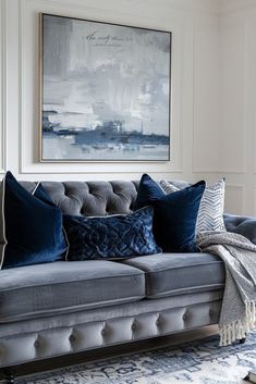 a gray couch with blue pillows in front of a painting on the wall above it