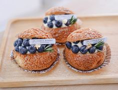 three pastries with blueberries and cream cheese on them sitting on a wooden tray