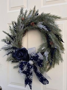 a christmas wreath on the front door with blue and silver bows hanging from it's side