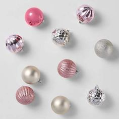 an assortment of christmas ornaments arranged on a white surface with pink and silver balls in the middle